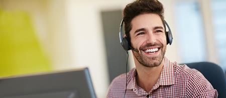 Man sitting at computer with headset on, smiling at someone off camera